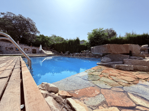 Piscina con entrada tipo playa de piedra, tarima de madera y escaleras de acero en chalet Las Pajanosas, Guillena.