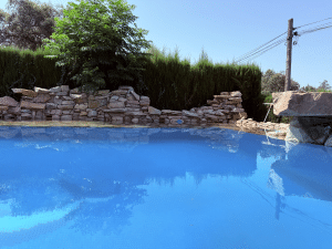 Piscina de aguas azules con borde de rocas naturales y setos altos en chalet en Las Pajanosas, Guillena