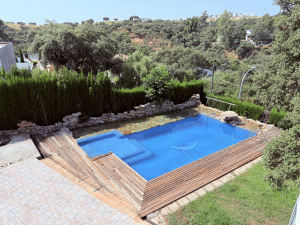 Piscina privada con escalones, rodeada de tarima de madera, césped y vegetación, en chalet en Las Pajanosas, Guillena.