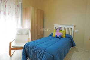 Dormitorio individual con cama, armario de madera y silla en chalet adosado en Alcalá del Río.