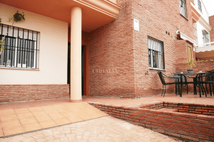 Patio delantero con rampa de acceso a garaje, zona de estar y fachada de ladrillo en chalet en Alcalá del Río.