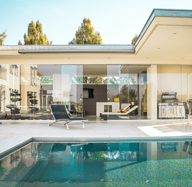 El patio trasero de una casa moderna con una piscina, una terraza con muebles de exterior y una cocina al aire libre.